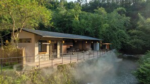 A traditional-style building with a wooden deck overlooking a river, surrounded by lush greenery. - Xiyang Yishan Quiet Private Onsen Country Style Vacation Courtyard (Qingyuan)
