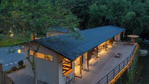 A modern house with a large deck, a dining area, and a view of a river. - Xiyang Yishan Quiet Private Onsen Country Style Vacation Courtyard (Qingyuan)