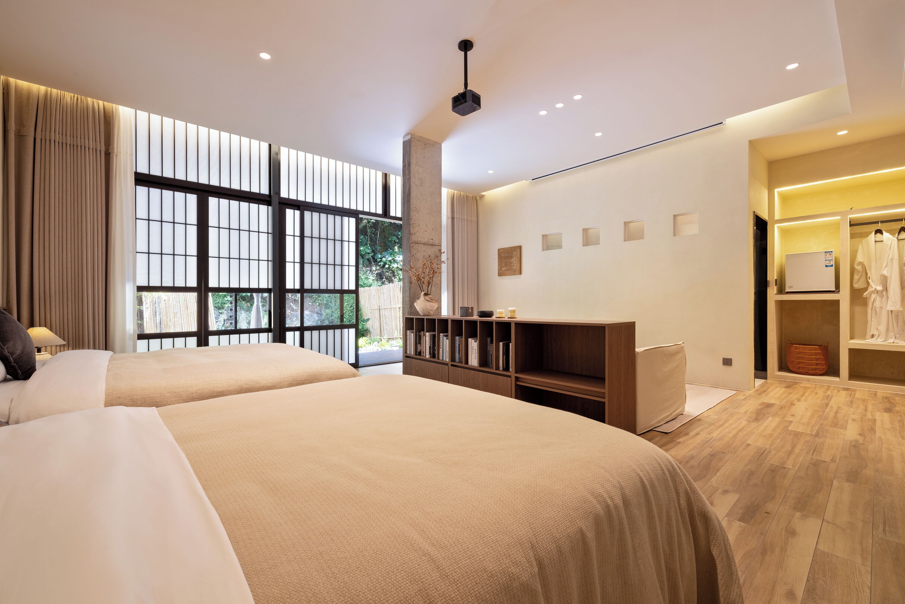 Habitación de hotel moderna con dos camas grandes, piso de madera, un ventanal con vistas a zonas verdes, un armario y una pequeña zona de estar.