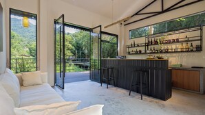 A modern kitchen with a bar area, a white sofa, and a view of greenery outside. - Xiyang Yishan Quiet Private Onsen Country Style Vacation Courtyard (Qingyuan)