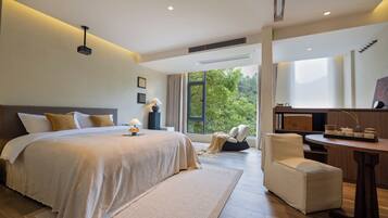 A modern bedroom with a large bed, a bedside table, a chair, and a view of greenery outside.