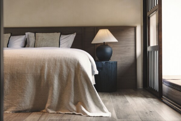 Una cama bien hecha con una colcha color beige, una lámpara de noche y un cabecero de madera.