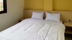 A hotel room with a bed, white bedding, and a yellow accent wall. - Slara Hostel Syariah 1 (Bandar Lampung)
