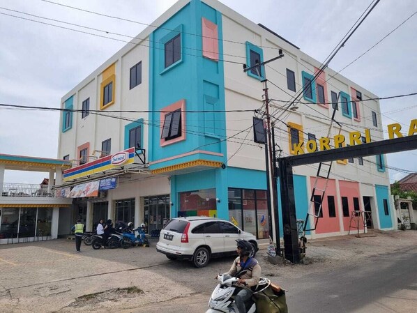 A multi-story building with a colorful facade, a visible sign for 'KORPRI', and a parked car and motorcycle in front.