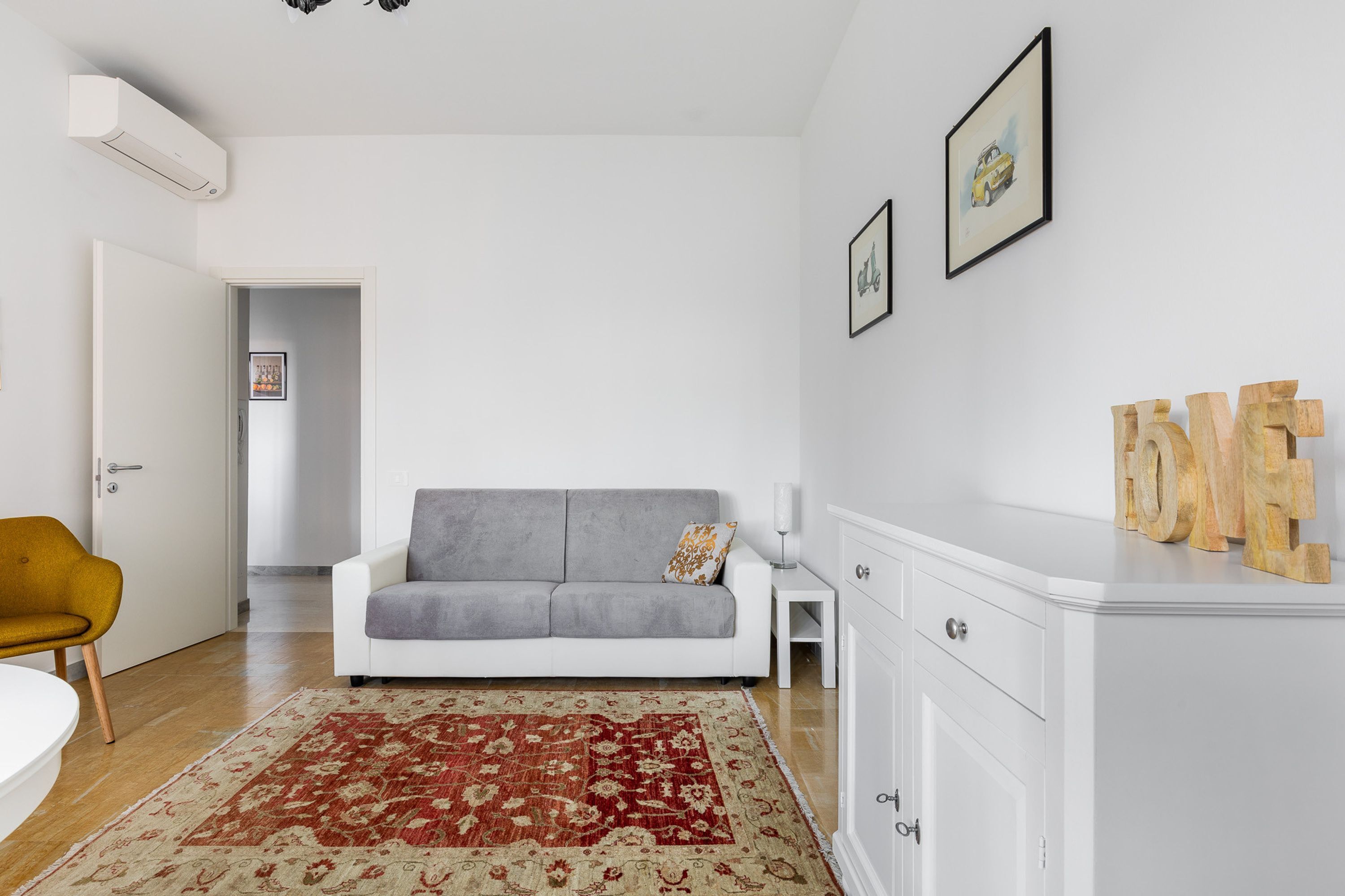 A modern living room with a grey sofa, a red and beige rug, a white cabinet, and a yellow chair.