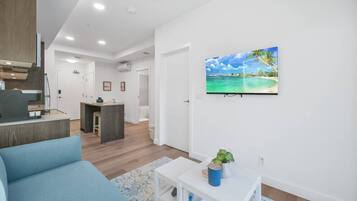 A modern living room with a blue sofa, a small white table with a plant, and a kitchen area in the background.