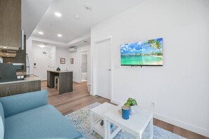 Ein modernes Wohnzimmer mit einem blauen Sofa, einem kleinen weißen Tisch mit einer Pflanze und einer Küchenzeile im Hintergrund.