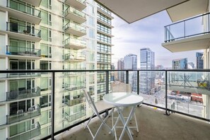 Um edifício alto com várias varandas, guarda-corpo de vidro e uma mesa com cadeiras.
