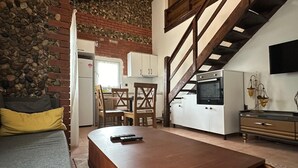 A spacious living area with a wooden dining table, a sofa, and a staircase leading to an upper level. - Kampüs Garden (Fethiye)