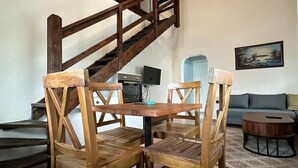 A wooden dining table with four chairs, a staircase, a television, and a painting on the wall. - Kampüs Garden (Fethiye)