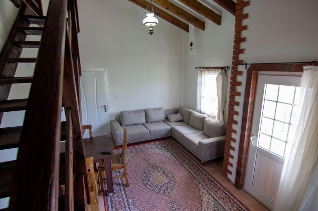 A living room with a grey sofa, a patterned rug, a wooden staircase, and a door with a brick accent.