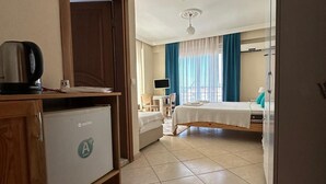 A hotel room with a bed, a desk, a chair, a TV, and a minibar. - Kampüs Garden (Fethiye)