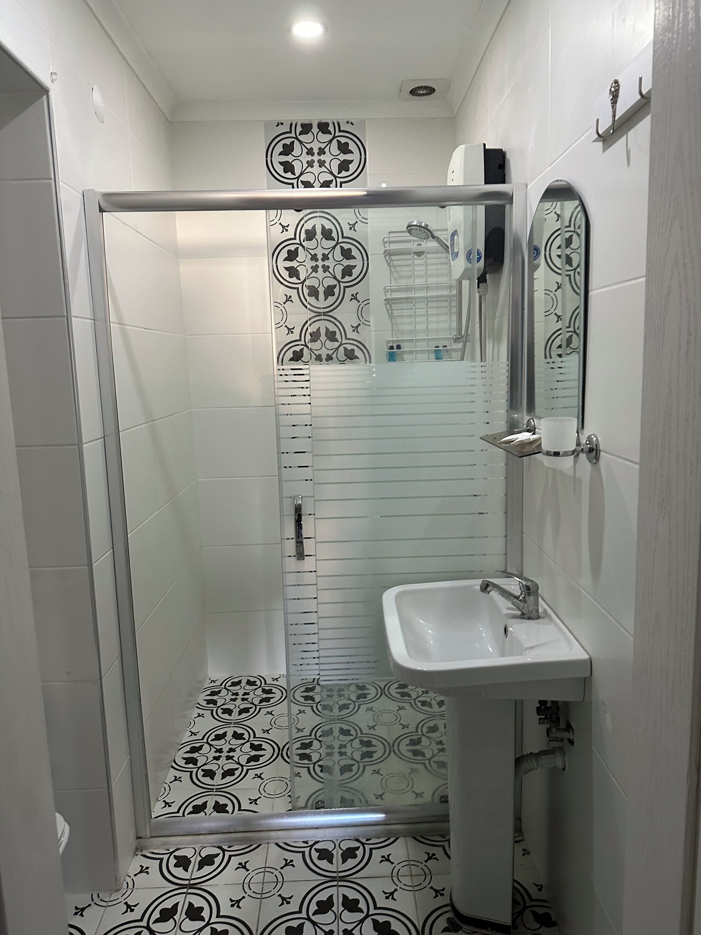 A bathroom with a glass shower enclosure, a sink with a mirror, and patterned floor tiles.