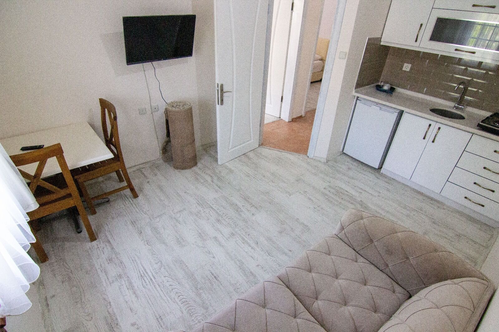 A compact living space with a dining area, a sofa, a kitchen, and a TV mounted on the wall.