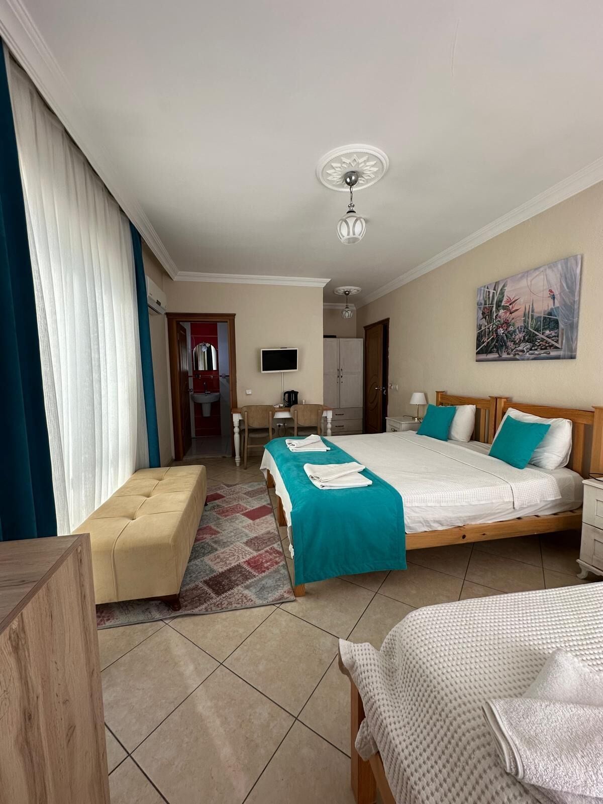 A hotel room with a bed, a desk, a chair, a television, and a painting on the wall.