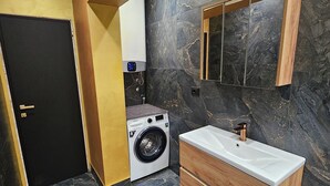 Un baño moderno con piso de mármol, lavadora, tocador de madera con lavamanos y un espejo grande.