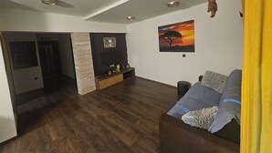 Un amplio salón con piso de madera oscura, pared de acento de piedra, televisor de pantalla plana montado en un panel negro y un cuadro de un atardecer.