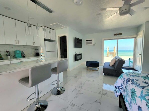 A modern kitchen with white cabinets, a bar area, a sofa, and a bed with a view of the ocean.