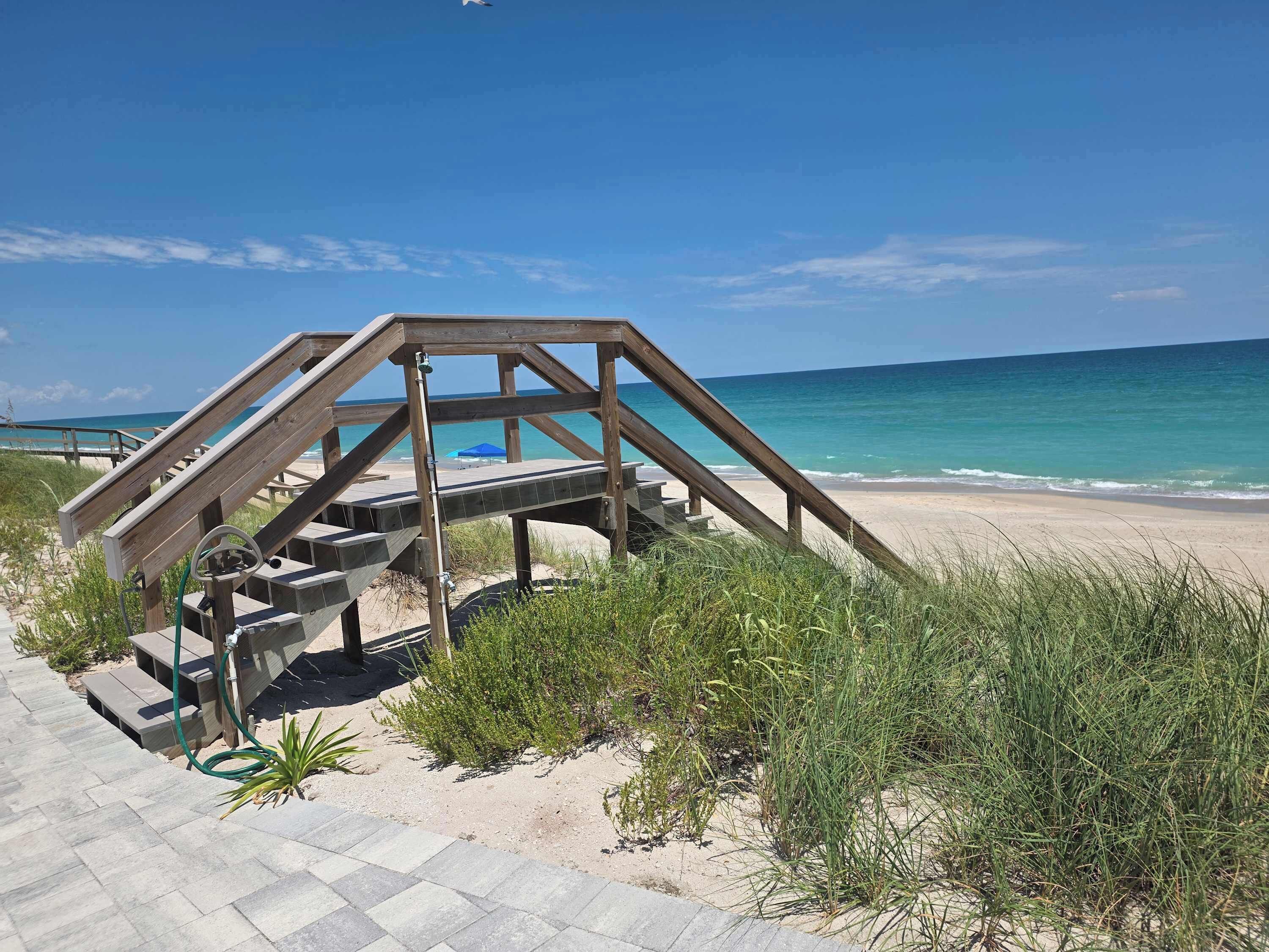 Une structure en bois avec un escalier menant à une zone de plage, entourée de sable et de végétation.