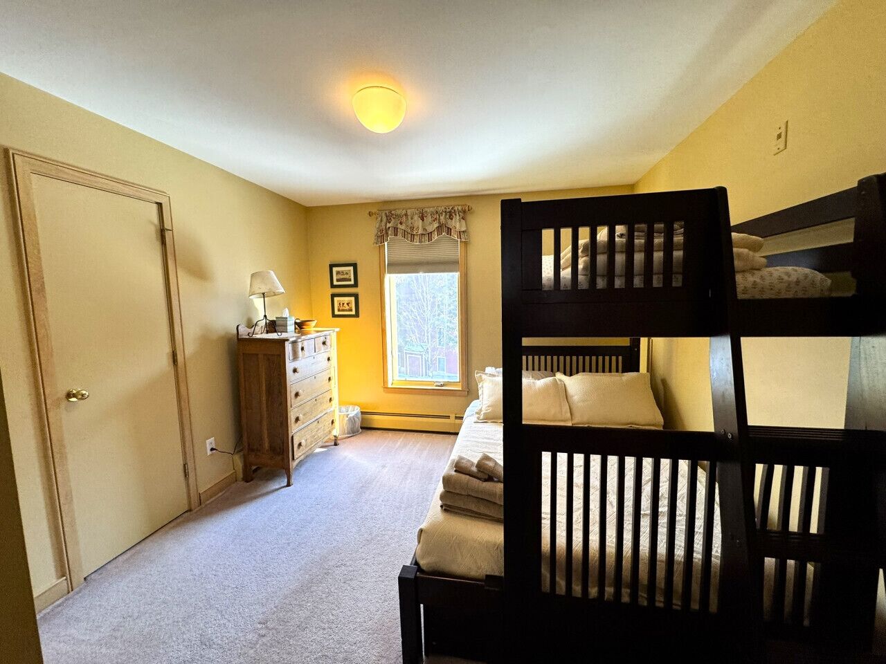 A bedroom with bunk beds, a dresser, a lamp, and a window with a view.