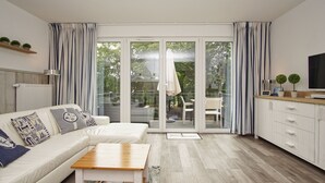 A modern living room with a sofa, coffee table, and a sliding glass door leading to an outdoor patio. - Residenz Waldidyll FeWo Kleiner Stubber - with use of the swimming pool at AHOI Sellin (Sellin)