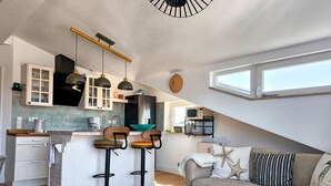 A modern kitchen with a central island, bar stools, a dining area with a sofa, and a small table with a candle. - Vacation at the Baltic Sea - Strandresidenz Lehrer Lämpel FeWo Anna Mari (Glowe)