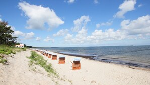A beach with rows of wooden beach chairs and a building in the background. - Vacation at the Baltic Sea - Strandresidenz Lehrer Lämpel FeWo Anna Mari (Glowe)