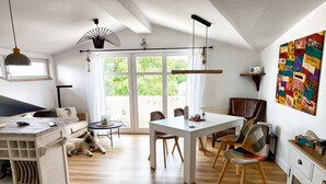 A bright, open-plan living space with a dining area, a sofa, a dog, and a large window. - Vacation at the Baltic Sea - Strandresidenz Lehrer Lämpel FeWo Anna Mari (Glowe)