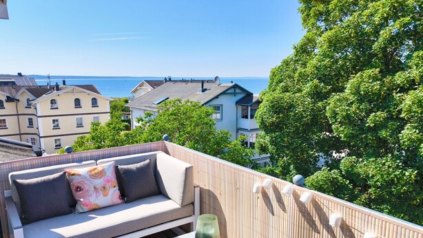 A balcony with a sofa and a small table, overlooking a coastal town and the sea. - Vacation at the Baltic Sea - Strandresidenz Lehrer Lämpel FeWo Anna Mari (Glowe)