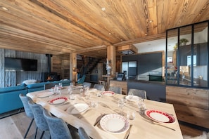A modern dining area with a wooden ceiling, a fireplace, and a view of the kitchen.