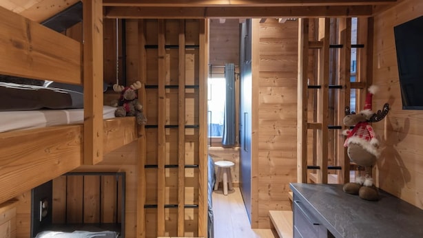 Un intérieur compact en bois, comprenant un lit superposé, un petit tabouret et un coin cuisine.
