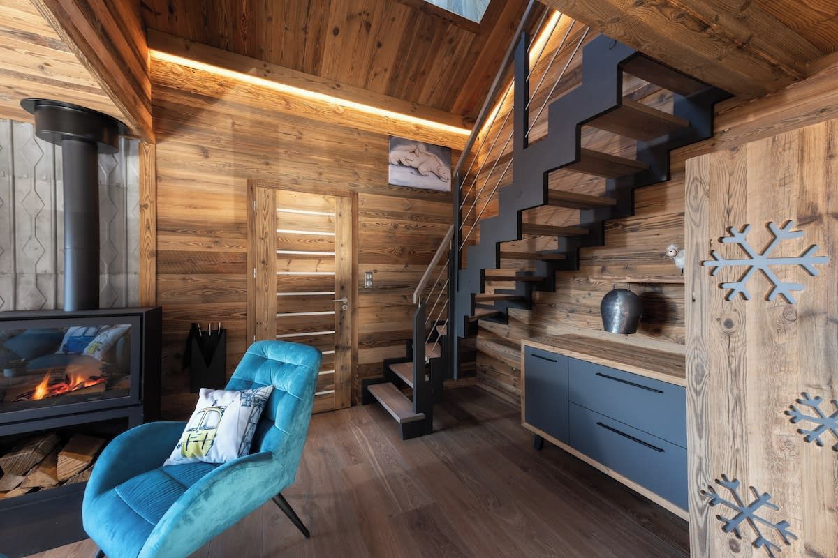 Ein modernes Interieur mit einer Holztreppe, einem Kamin und einem blauen Sessel.
