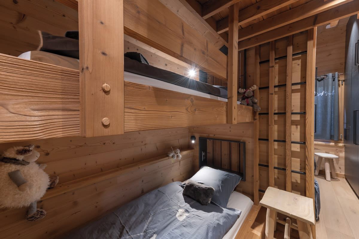 A wooden cabin interior with bunk beds, a small table, and a shelf with stuffed animals.