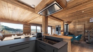 Une cuisine moderne dotée d’un îlot central, d’un plafond en bois et de grandes fenêtres offrant une vue sur l’extérieur.