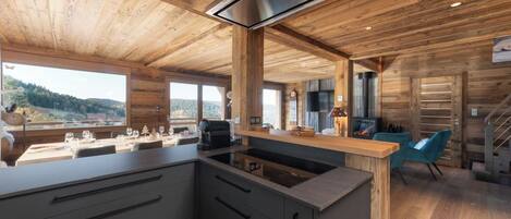 Cocina moderna con una isla central, techo de madera y grandes ventanales con vistas al exterior.