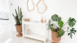 Una consola blanca con adornos, dos espejos de pared y plantas en macetas.