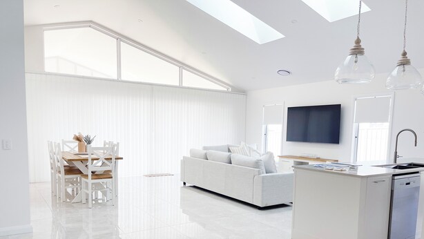 Una cocina moderna con lavavajillas integrado, un comedor con mesa y sillas blancas, y un ventanal que proporciona luz natural.