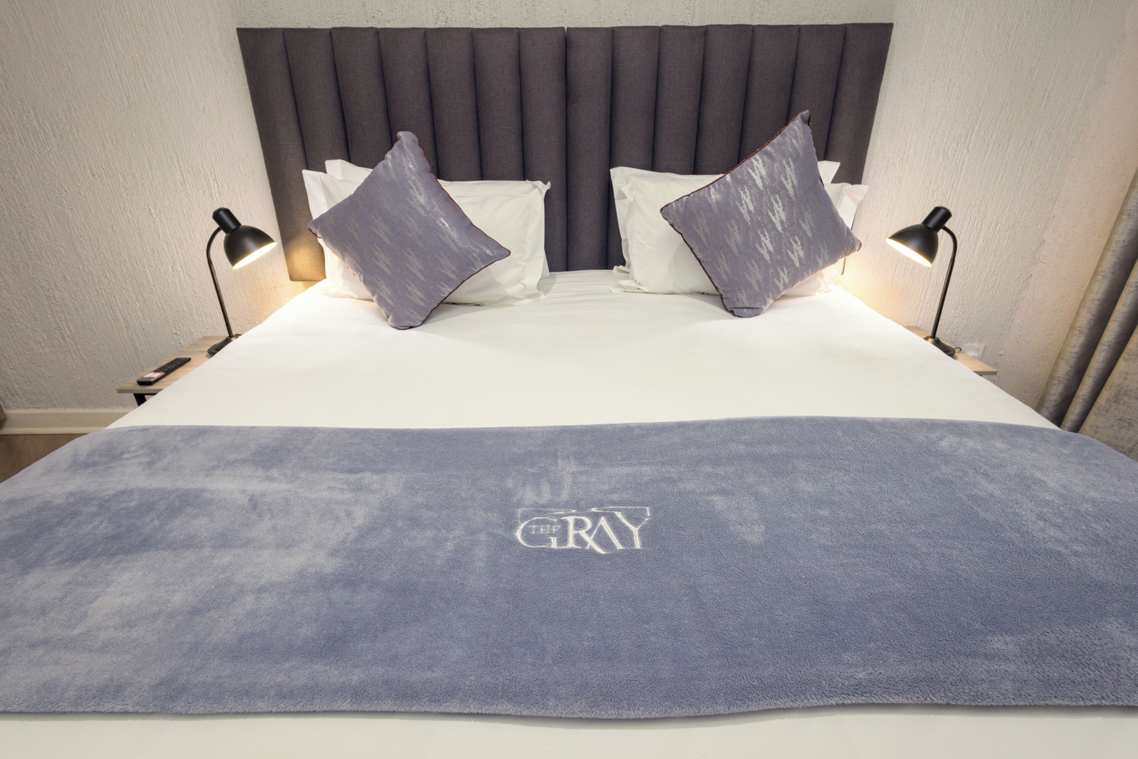 Una cama con cabecera gris, dos almohadas y una manta con la palabra 'GRAY' bordada.
