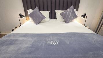 Una cama con cabecera gris, dos almohadas y una manta con la palabra 'GRAY' bordada.
