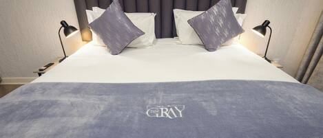 A bed with a gray headboard, two pillows, and a blanket with 'GRAY' embroidered on it.