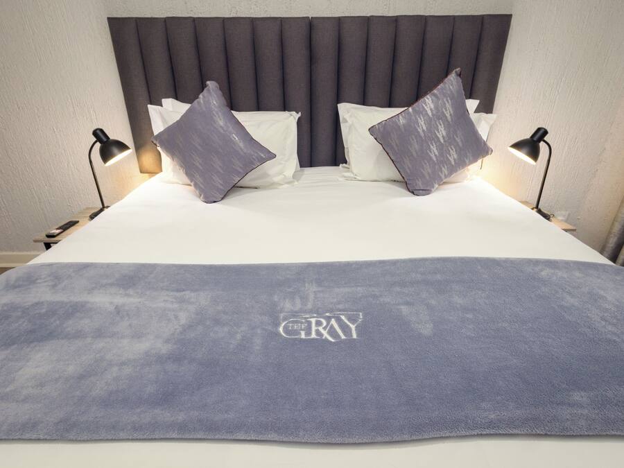 A bed with a gray headboard, two pillows, and a blanket with 'GRAY' embroidered on it.