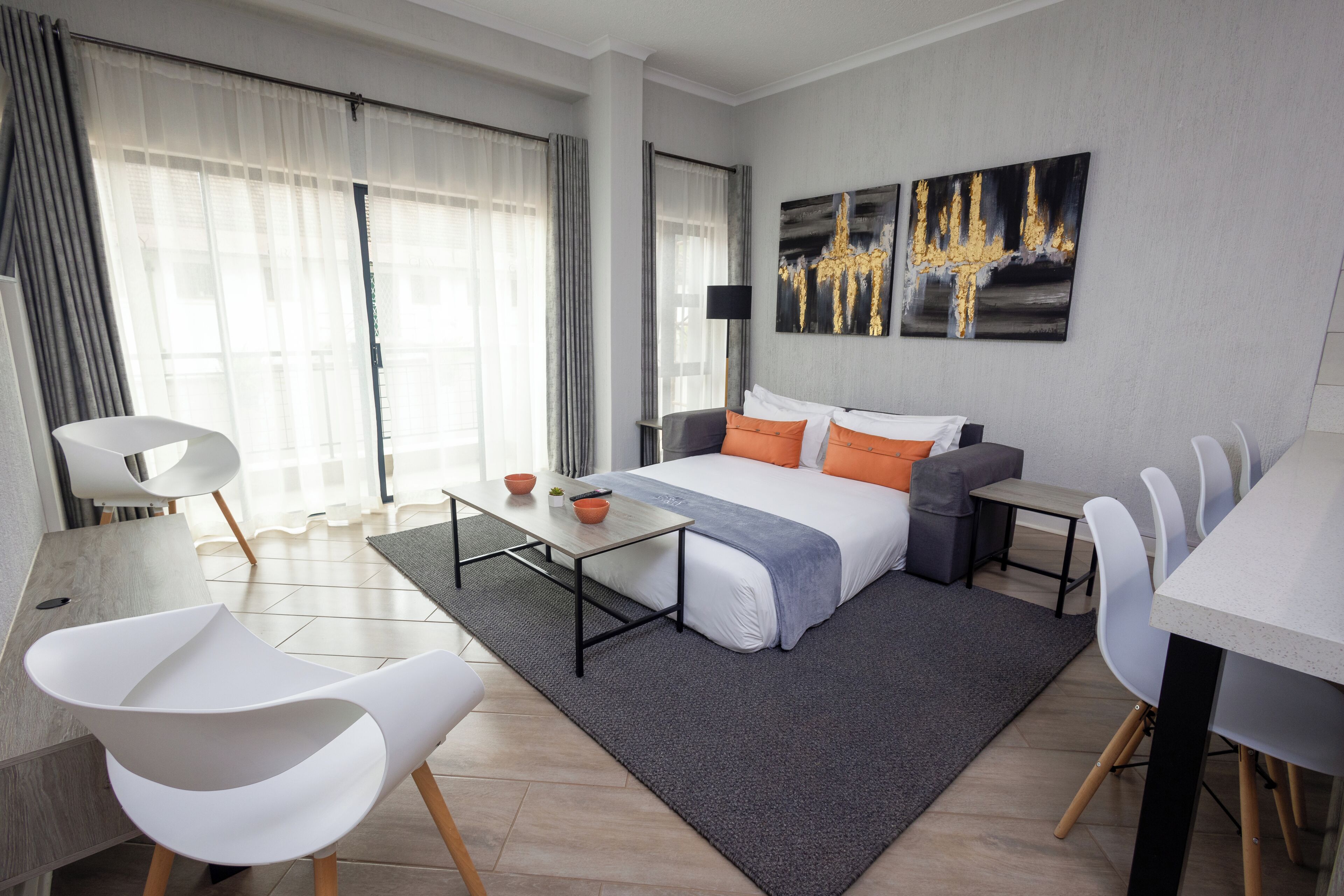 A modern hotel room with a bed, a desk, a chair, a dining table, and a large window with curtains.