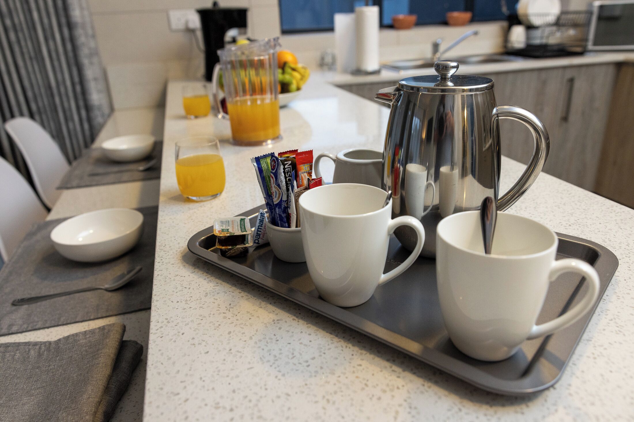 A breakfast tray with coffee pot, cups, and juice on a kitchen counter.