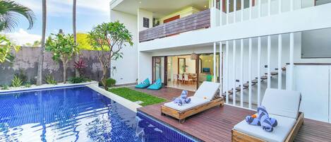 Una casa moderna de dos pisos con piscina, sillones de descanso y zona de comedor.