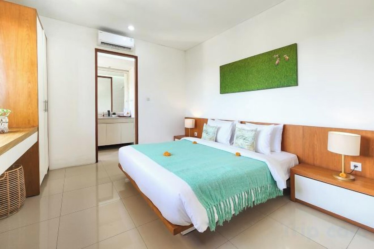 A hotel room with a bed, bedside tables, a mirror, and a green wall decoration.