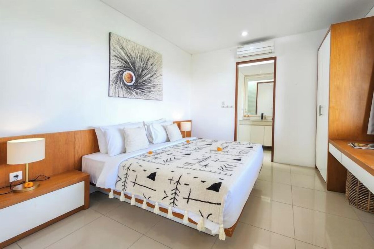 Una habitación de hotel con cama, mesita de noche, lámpara y un cuadro abstracto grande en la pared.