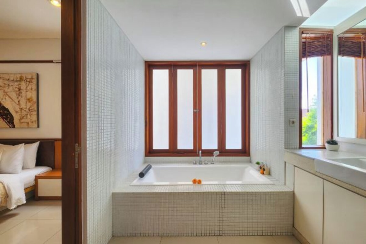 A modern bathroom with a large bathtub, a window with wooden shutters, and a tiled floor.