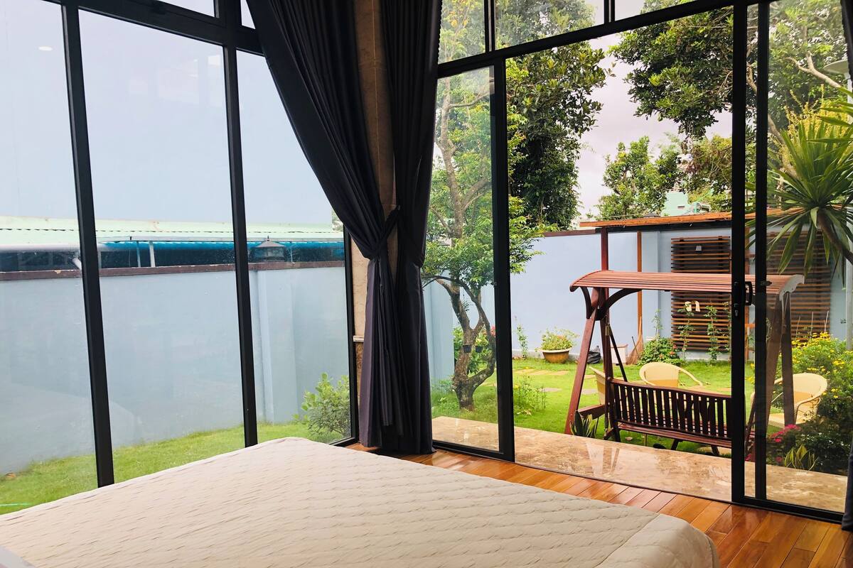 Un dormitorio con un amplio ventanal con vistas a un jardín y una masa de agua.