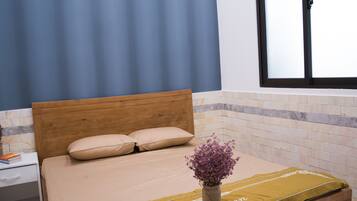 Un dormitorio con cama de madera, una mesita de noche, un florero con flores y una ventana con persianas.