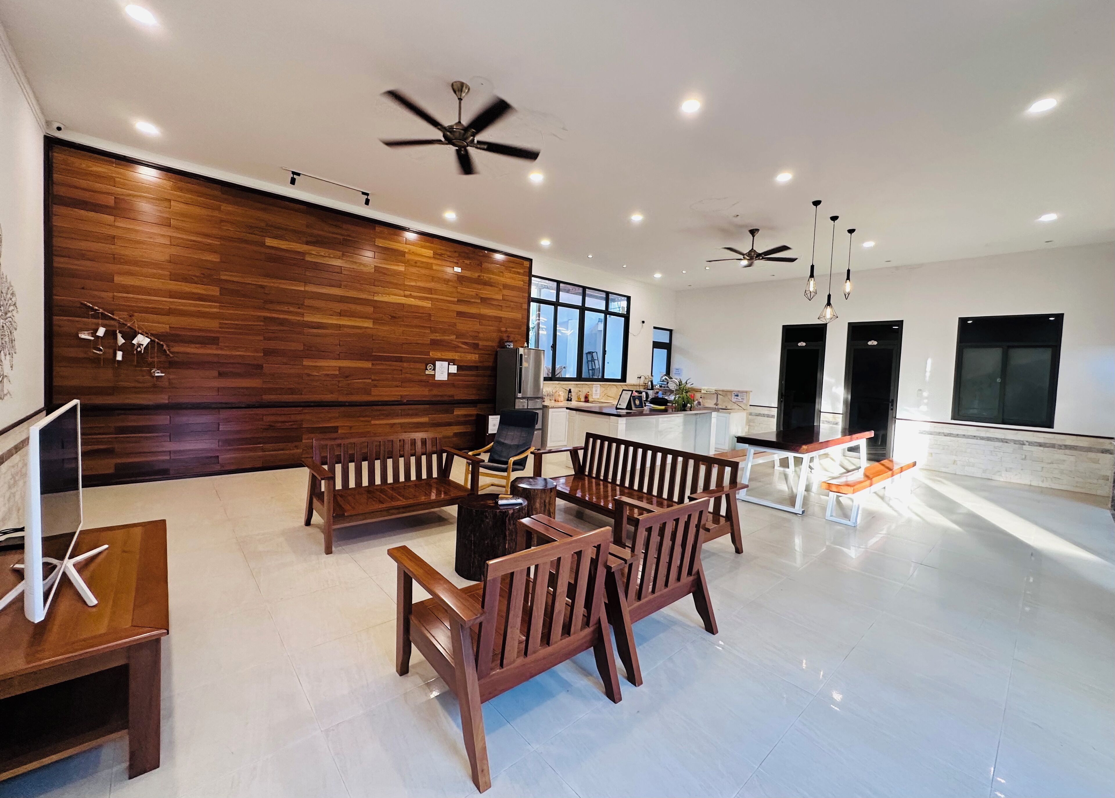 Amplia sala de estar con pared de madera, mesa de comedor con sillas y ventiladores de techo.